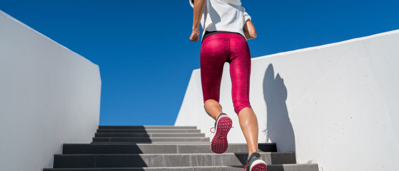 Stairs climbing running woman doing run up steps on staircase. Female runner athlete going up stairs in urban city doing cardio sport workout run outside during summer. Activewear leggings and shoes.