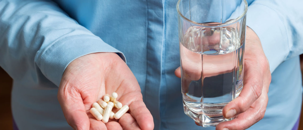 White medication capsules of glucosamine, healthy supplement pills in woman palm hand and glass with water in the other hand.